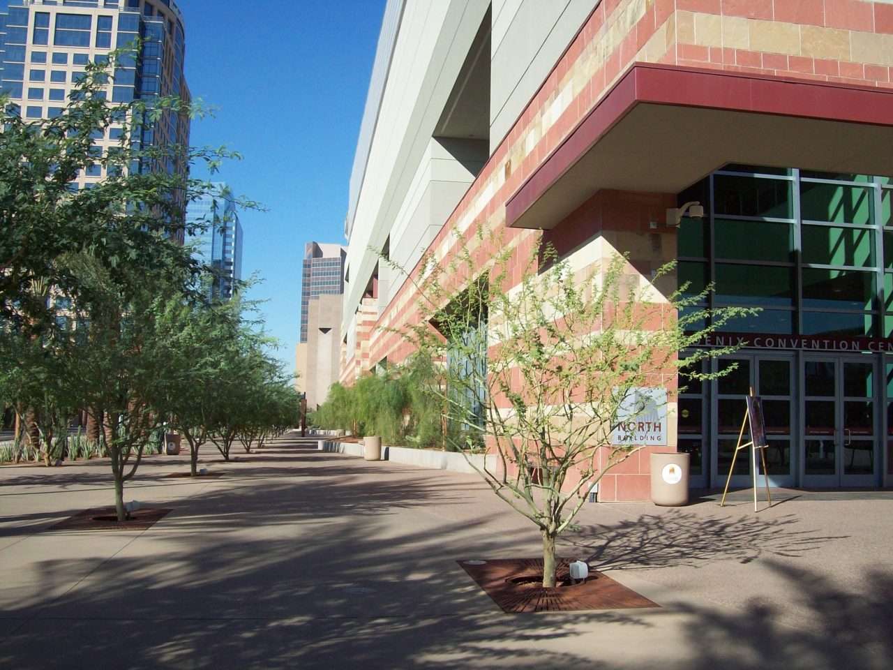 A shaded downtown sidewalk passes newly planted desert trees at the Phoenix Convention Center entrance.