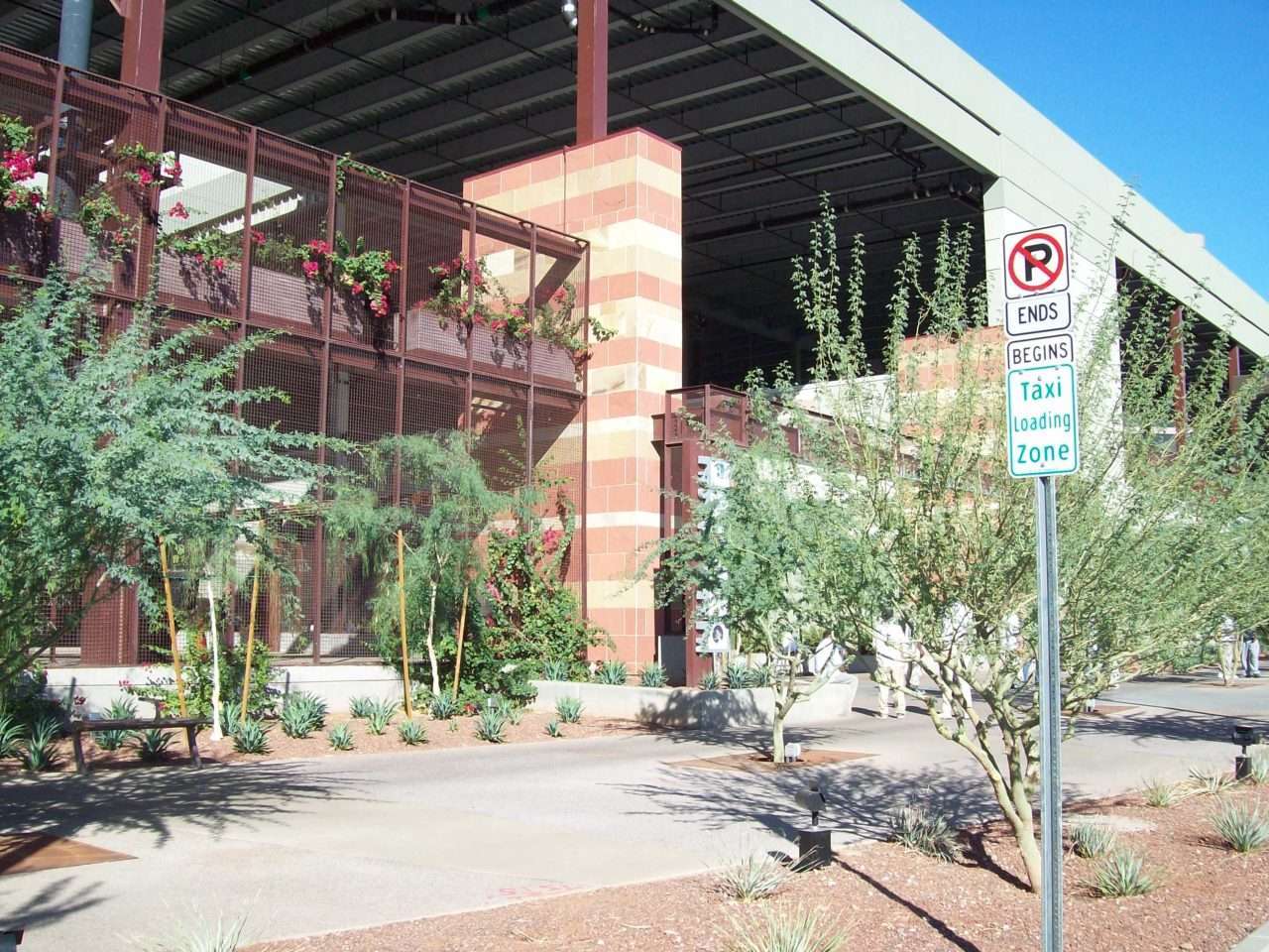 Desert trees, flowering plants, and sculptural metalwork frame a convention center entrance.