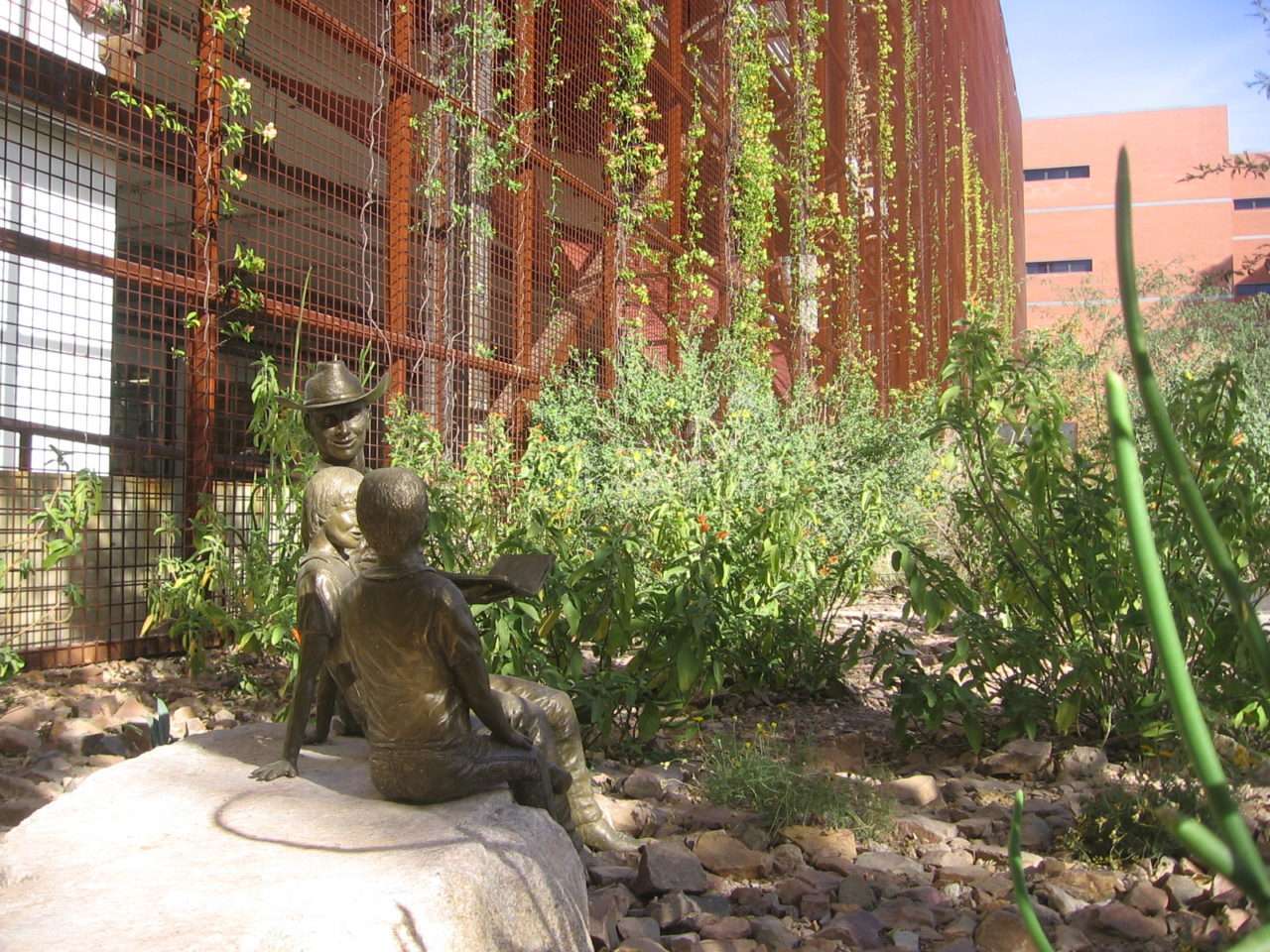 A bronze figure sits among desert plants, vines, and tall succulents in Underwood Garden.